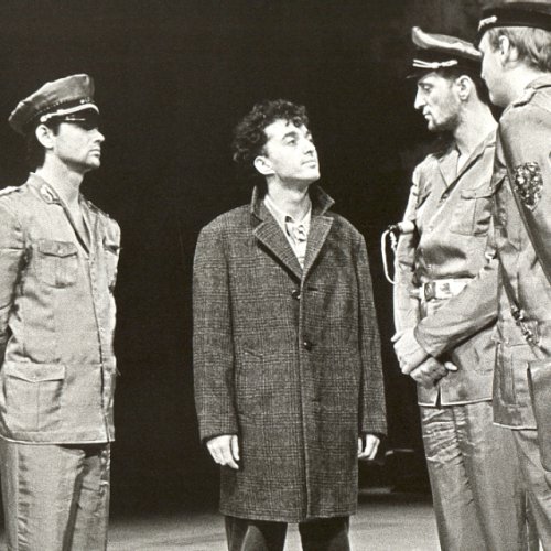 Das Foto zeigt eine Szene aus dem Theaterstück "Wer ist Paule Panke?". André in der Rolle des Paule wird hier von 3 Schauspielern umstanden, die stilisierte Polizeiuniformen tragen.