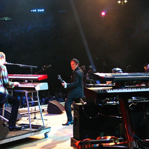 Blick vom Bühnen-Rückraum auf die Band in Richtung Publikum, mit Keyboards im Vordergrund